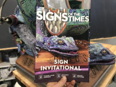Signs of the Times Magazine cover showing sign sculpture held in front of actual sculpture